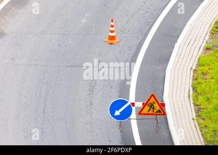 Turn left sign on the road. Warning signs and orange safety traffic cones on background. Direction of detour, roadworks. Road signs denoting road repa Stock Photo