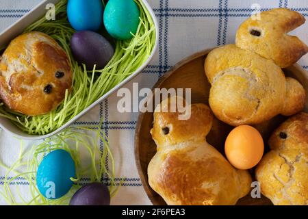 Sweet brioche dough in the shape of Easter bunnies, a basket with edible Easter grass and colored Easter eggs. Stock Photo