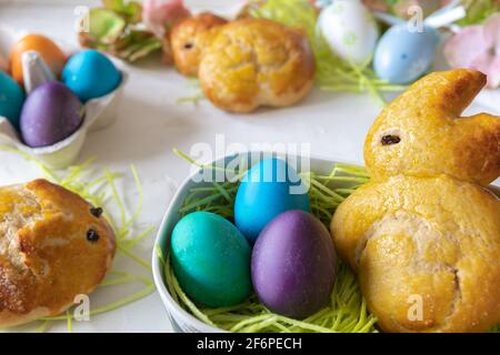 Sweet brioche dough in the shape of Easter bunnies, a basket with edible Easter grass and colored Easter eggs. Stock Photo