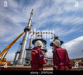 Aktau, Kazakhstan - May 19, 2012 Construction of asphaltic bitumen plant refinery column. Metal distillation tower, two workers and yellow mobile cran