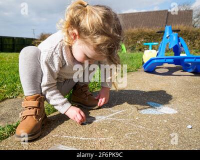 Toddler drawing with chalk on path in garden, UK Stock Photo