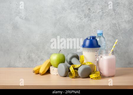Protein cocktail, dumbbells, measuring tape, water bottle and fresh fruits on wooden table Stock Photo