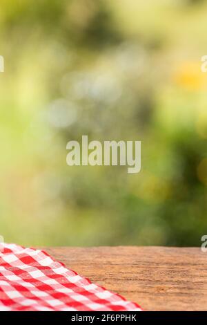 Checkered red napkin on wooden table against green blurred background. Space for design Stock Photo