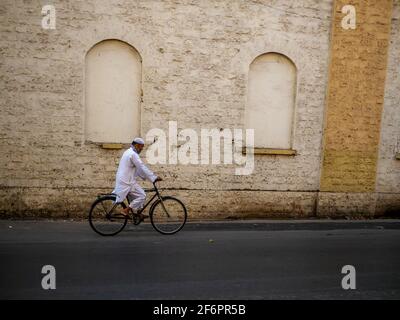 Mumbai, India - January 7, 2021 : Muslim old age man wearing traditional Islamic clothes and skull cap riding a bicycle on the streets of Mumbai Stock Photo