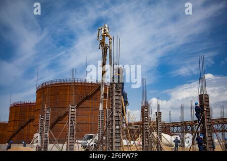 Aktau, Kazakhstan - May 19, 2012 Construction of modern asphaltic bitumen plant.  Rusty oil storage tank. Making building columns. Workers on form. Ru