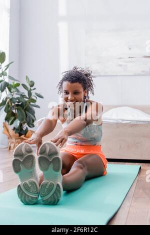 Smiling african american woman stretching on floor in bedroom Stock Photo