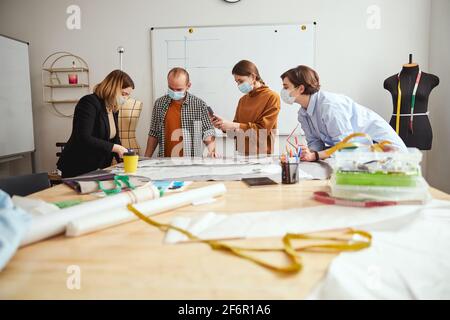 Three people watching a dress designer cutting fabric Stock Photo
