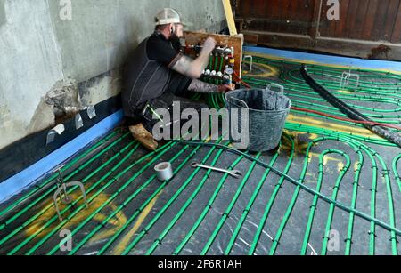 Workman setting up and testing pipework for underfloor heating system before anhydrite floor screed is poured on top Stock Photo