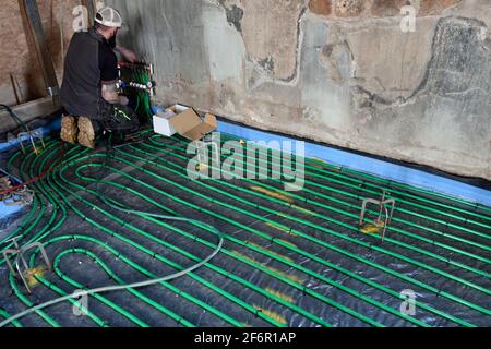 Workman setting up and testing pipework for underfloor heating system before anhydrite floor screed is poured on top Stock Photo