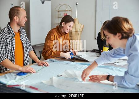 Cheerful couturiere laughing while cutting fabric material Stock Photo