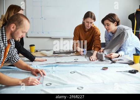 Woman tailor showing fabric sheet to co-worker while cutting Stock Photo
