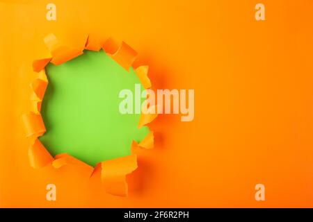 Torn hole and ripped of orange paper with space for text with green background. Stock Photo