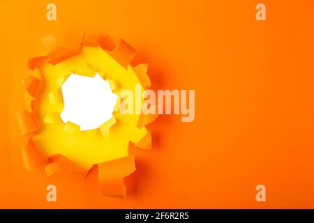 Torn hole and ripped of orange paper with space for text with white background. Stock Photo