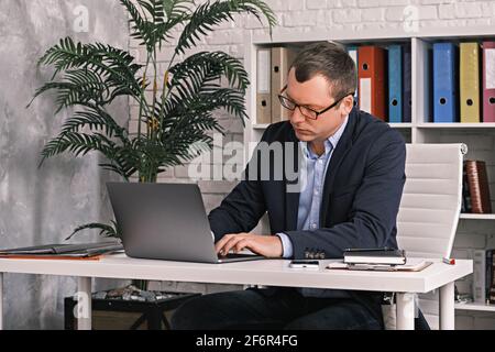 Man wearing suit and glasses typing something using laptop sitting at a desk in the office Stock Photo