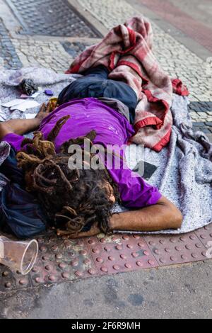 Drug addict Brazilian homeless sleeping on the sidewalk. Wearing dirty clothes and dreadlocks. Cocaine mirror on the side. Stock Photo