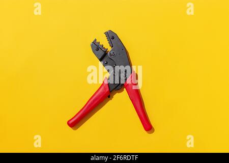 Tool, red crimping press pliers for electrical wiring on yellow background, flat lay with hard shadow for pattern. Stock Photo