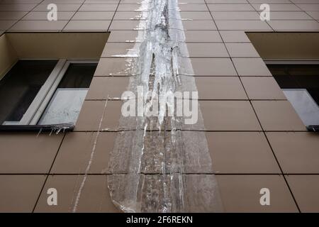 Frozen rain pipe on an apartment building. Ice on the building wall. Stock Photo