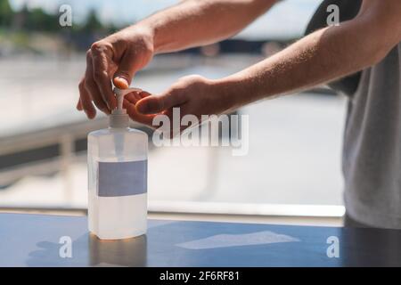 Person using hand sanitizer gel in public. Hand pressing antibacterial lotion bottle outside. Close up view of antiseptic being used in the street. Stock Photo