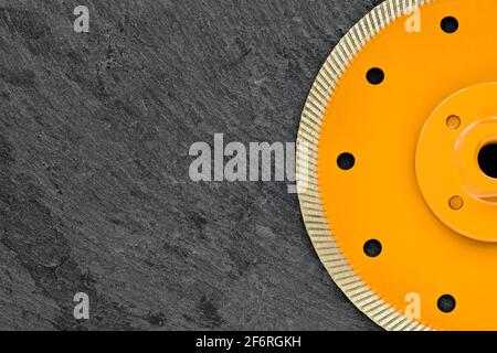 Half of a yellow diamond cutting wheel with a threaded nut on a dark gray granite background, the concept of stone processing in the interior. Stock Photo