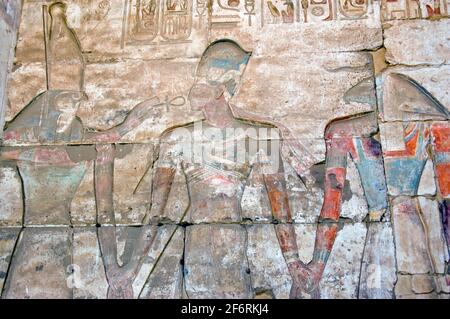 Ancient Egyptian hieroglyphic, painted carving showing the falcon headed god Horus and the goat headed creator god Khnum with the Pharoah Ramses II be Stock Photo