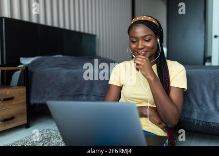 Video conference. Positive african woman having web call on laptop at home, wearing headset, gesturing and talking at camera, sitting on couch in livi Stock Photo
