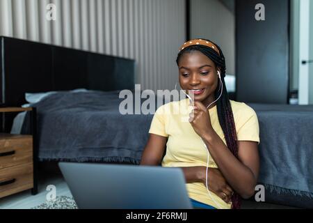 Video conference. Positive african woman having web call on laptop at home, wearing headset, gesturing and talking at camera, sitting on couch in livi Stock Photo