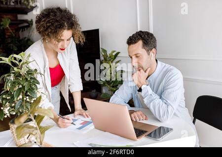 Serious coworkers discussing financial graphs, developing a project, doing paperwork. Concentrated business partners using laptop, working on new Stock Photo