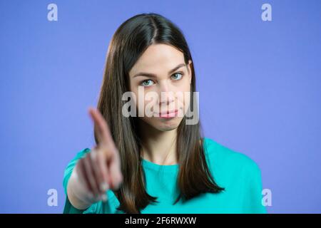 Portrait of serious woman showing rejecting gesture by stop finger sign. Girl isolated on violet background. Stock Photo