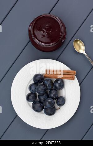 Fresh organic plums, cinnamon sticks and homemade jam in glass jar on gray table above view Stock Photo