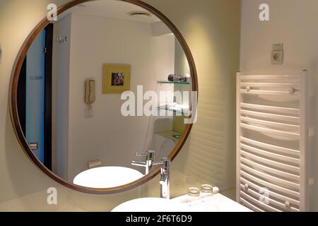 A large round mirror in the modern bathroom interior in an apartment or hotel, with the sink and faucet reflected Stock Photo