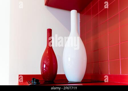 Red and white minimalist glass vases on the black glass ceramic hob or stove, against red background Stock Photo