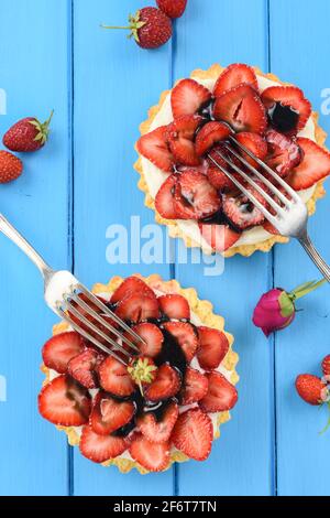 Two tartlets with fresh strawberries, mascarpone and licorice syrup with vintage forks on bright blue background above view Stock Photo