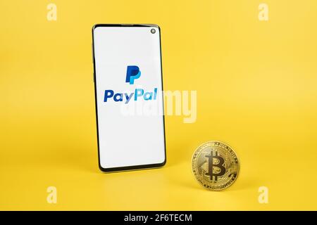 PayPal logo on phone screen with Bitcoin cryptocurrency coin on yellow background. Checkout with crypto, new payment option concept Stock Photo