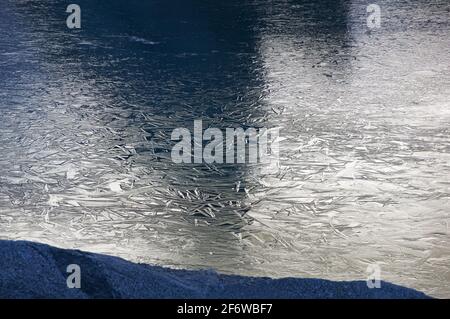 reflection of sunny rocks on ice crystals on an alpine lake in the Sierra Nevada Mountains Stock Photo