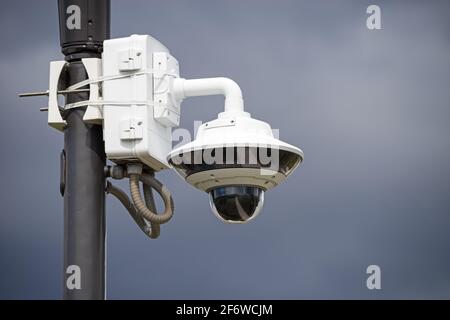 surveillance camera in a park mounted on a light pole with gray sky background Stock Photo