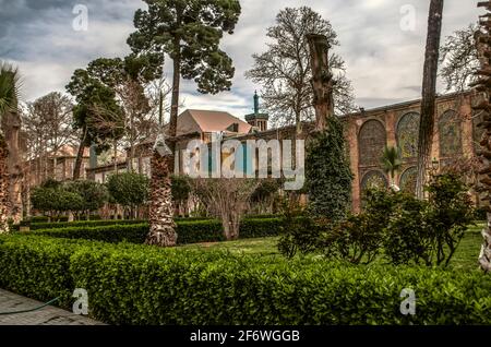 Palm trees wrapped for the winter, tall conifers and pruned old tree trunks on a green lawn fenced with evergreen bushes in the courtyard of the Goles Stock Photo