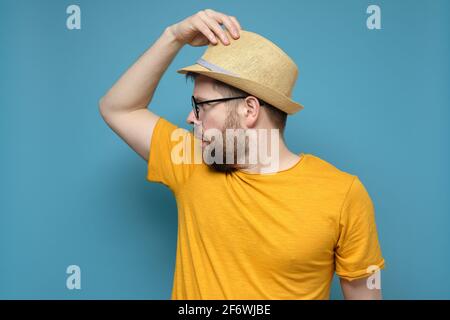 Strange, confused man in a straw hat makes a greeting gesture and surprise looks away. Blue background. Stock Photo