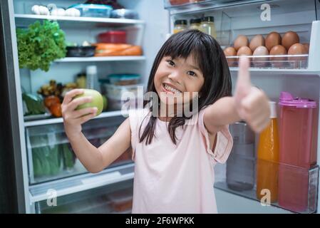 asian girl open fridge door drinking a bottle of juice Stock Photo