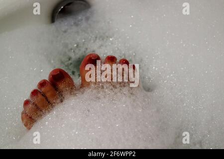 Close up of woman's red painted toe nails having a relaxing bubble bath Stock Photo