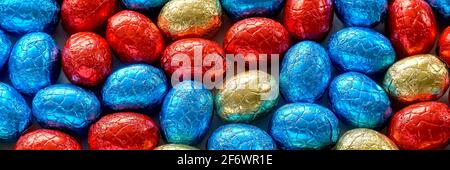 Closeup of many chocolate easter eggs wrapped in blue, red and golden foil. Easter banner background Stock Photo