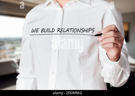 Businessman hand holds a pen and underlines the words we build relationships on a virtual screen. Business network or customer care satisfaction conce Stock Photo