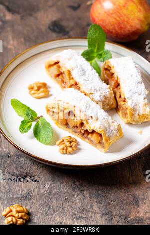 homemade fragrant strudel with apples and cinnamon on a plate on a wooden background with space for text, Stock Photo