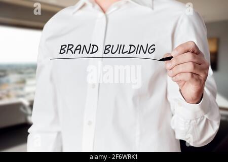 Businessman hand holds a pen and underlines the words brand building on virtual screen. Business marketing concept. Stock Photo