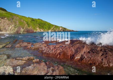 Beautiful red rocks Talland Bay Cornwall UK with blue sea and waves Stock Photo