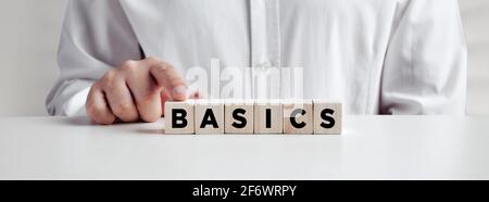 Businessman pressing his finger on the wooden cubes with the word basics. Back to basics, simplification in business or education concept. Stock Photo