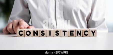 Businessman pressing his finger on the wooden cubes with the word consistency. Consistency in business or work concept. Stock Photo