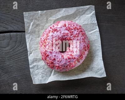 freshly baked pink donut on black wood background, top view Stock Photo