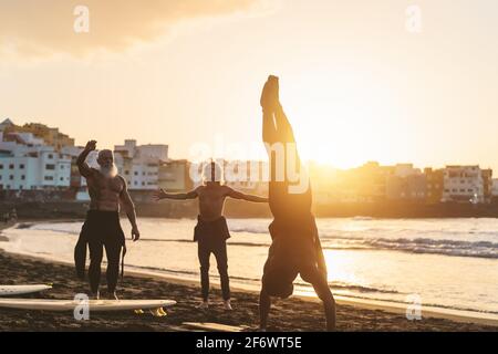 Happy fit surfers with different age and race doing warm up exercises before surfing during sunset time Stock Photo