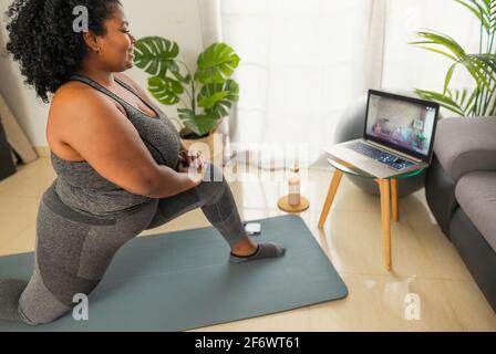Young African woman doing pilates virtual fitness class with laptop at home - Sport wellness people lifestyle concept Stock Photo