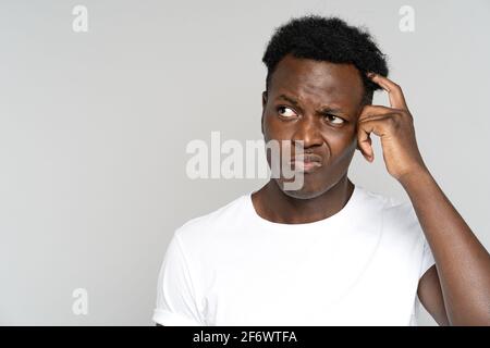 unsure doubtful African man scratching head, looking left doubtfully, plans or reconsiders something Stock Photo